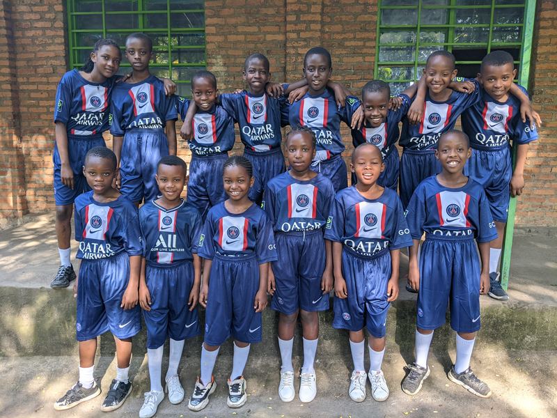 The school football team in matching kit, smiling on the steps outside a classroom block