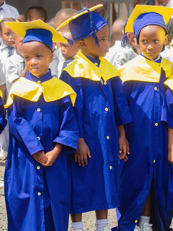 Three nursery pupils in blue and gold graduation gowns and caps