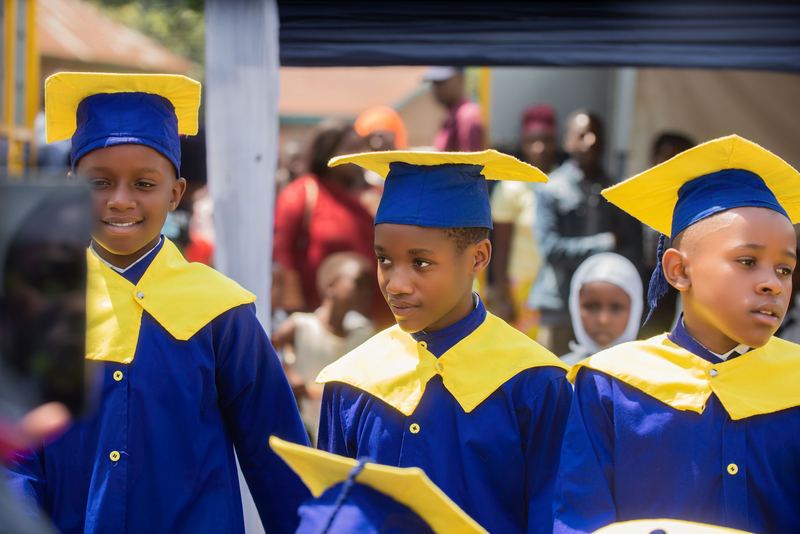 Three P6 pupils in blue and gold graduation gowns and caps on graduation day